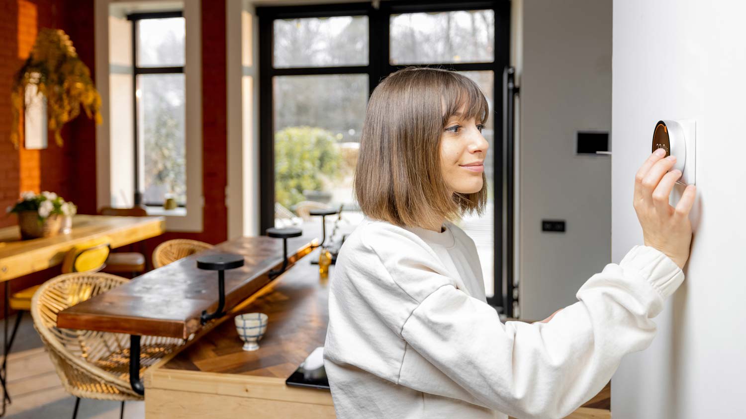 A young woman adjusting the temperature via a smart thermostat