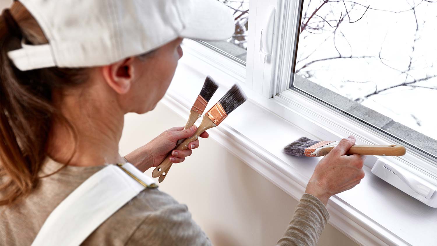 woman painting window trim with different brushes