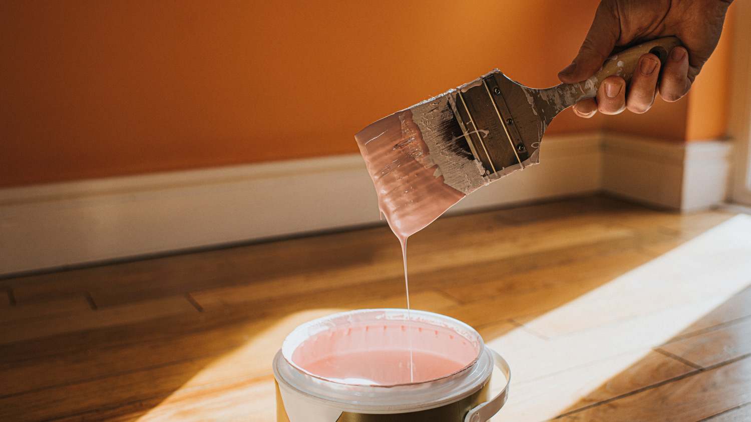 Hand dipping a paint brush into a large tin of pink paint