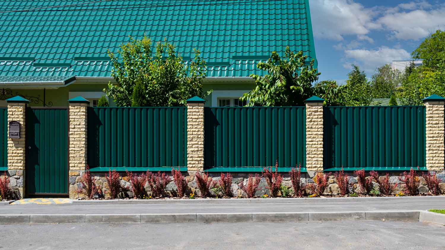 A green metal corrugated fence in front of a beautiful house