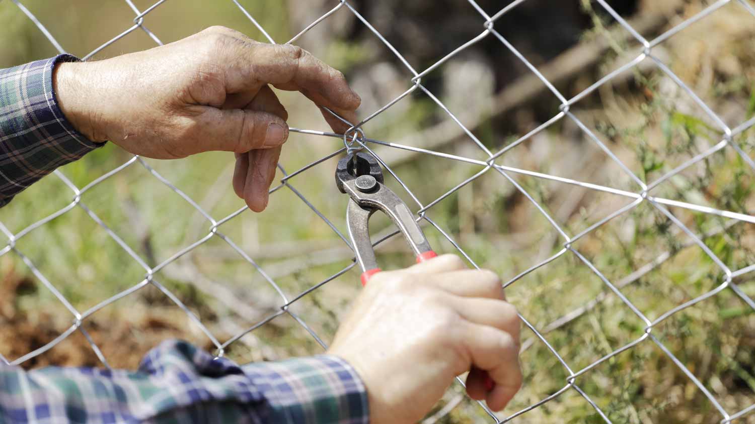 Close-up of a man repairing a chain link fence