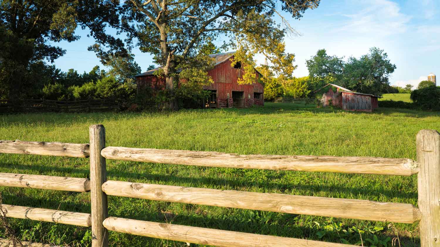 A red barn with a split rail fence on a summer day