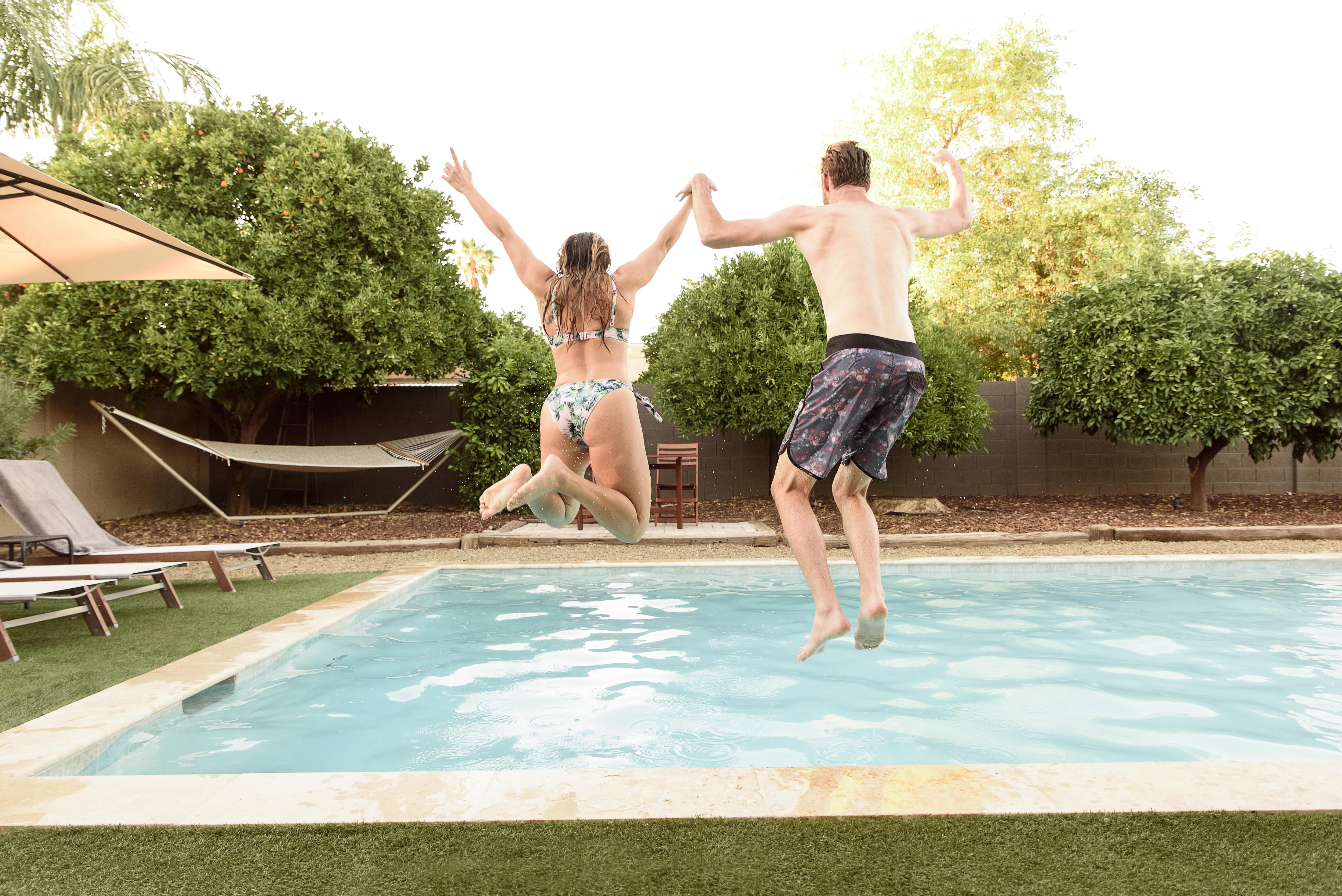 A man and woman jumping into a backyard inground pool together