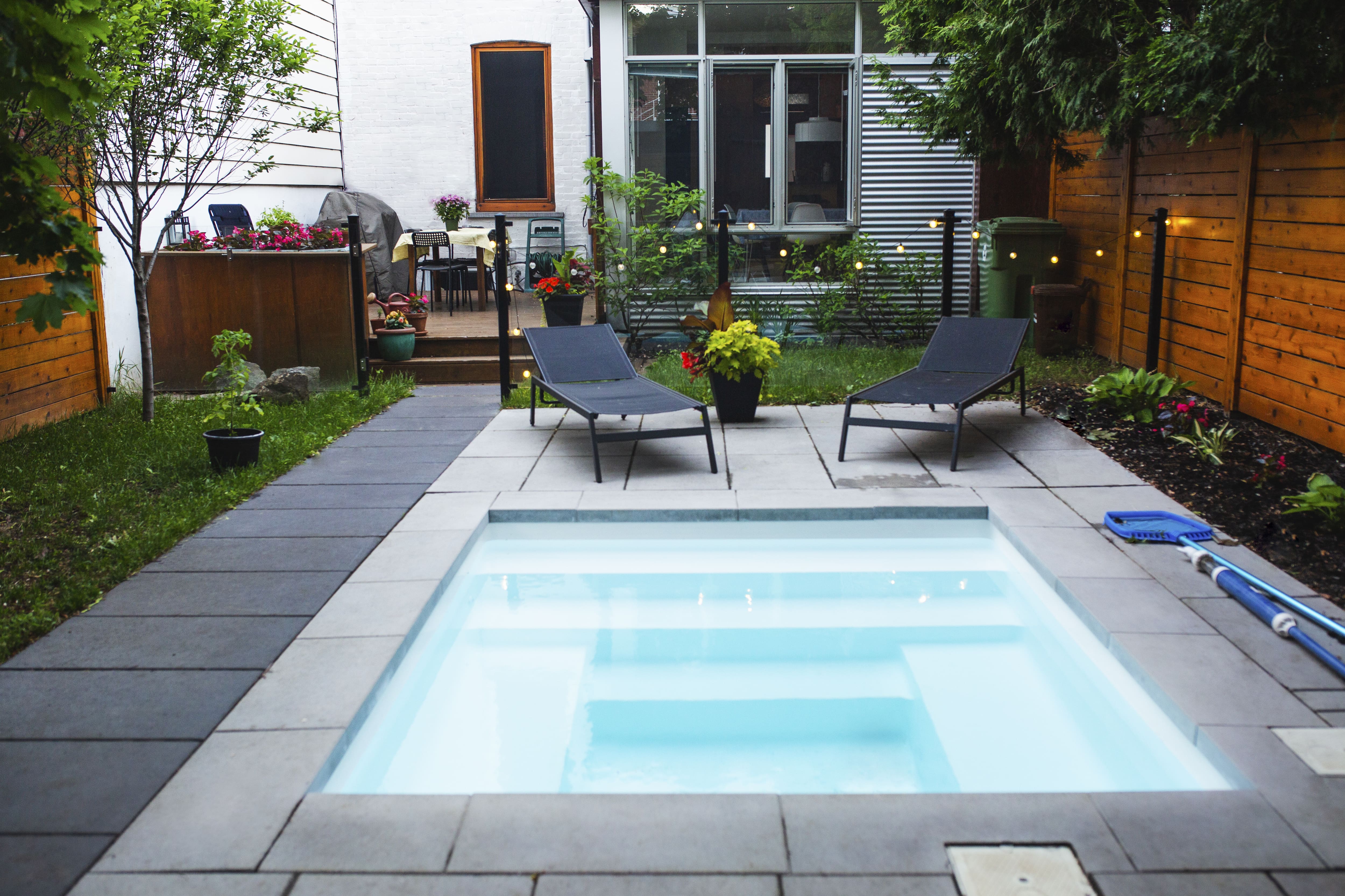 A small backyard with a small, square swimming pool surrounded by concrete tiles