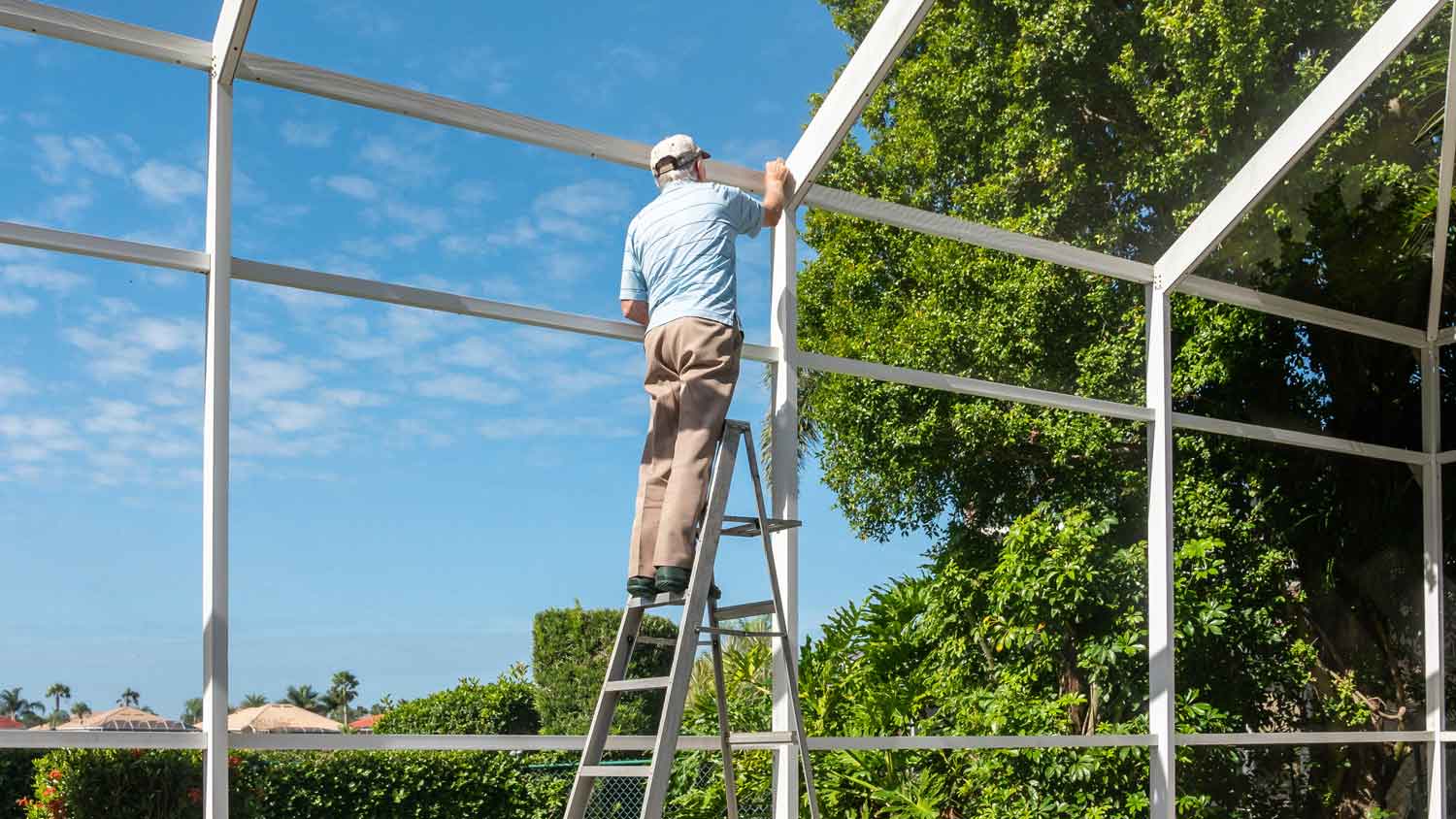 A man on a ladder constructing a pool enclosure
