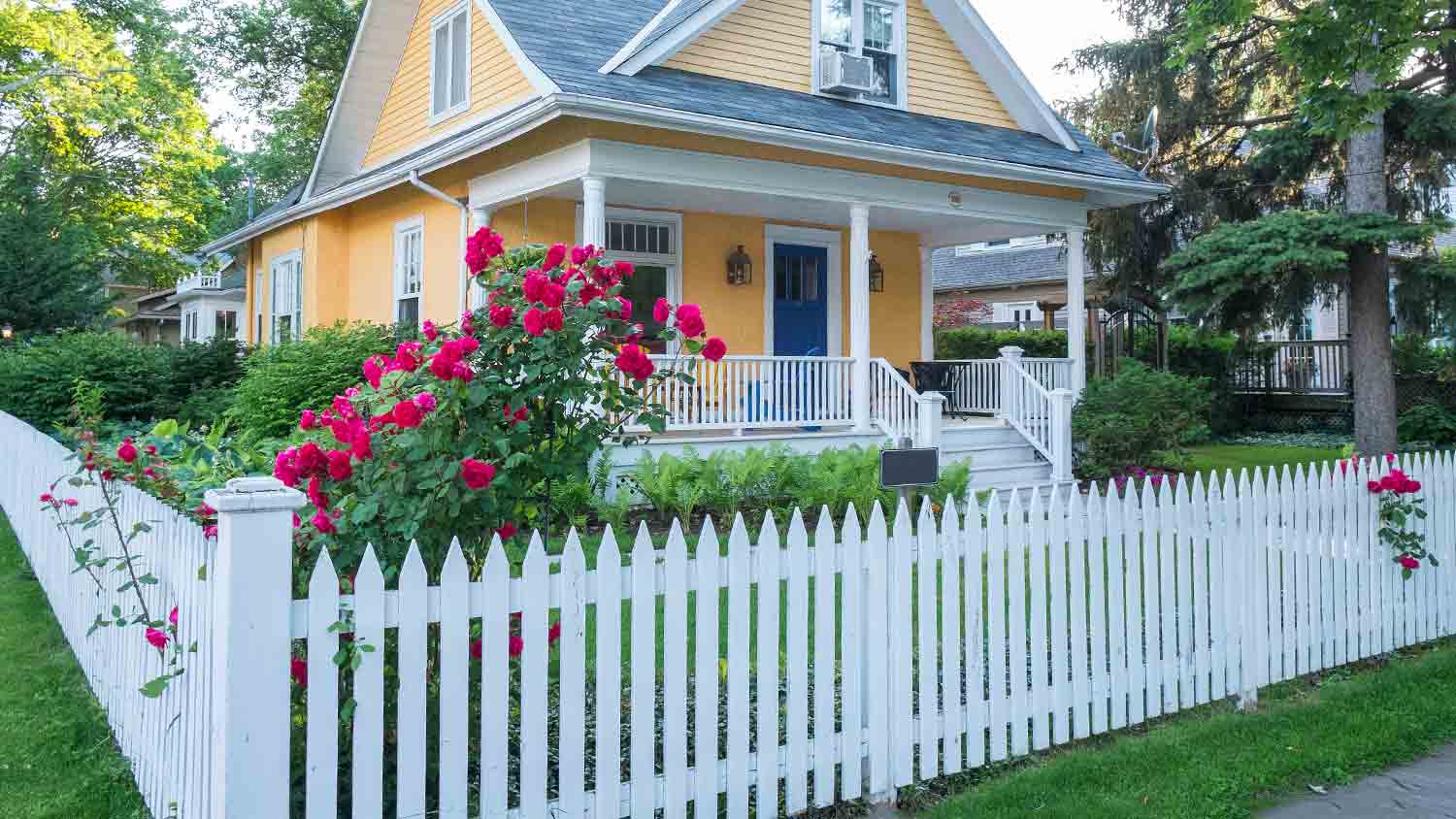 white picket fence in front of yellow house