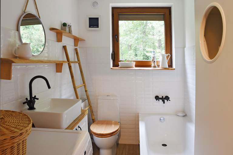 shot of small bathroom with white tile, white sink, bathtub and toilet, and tan accents