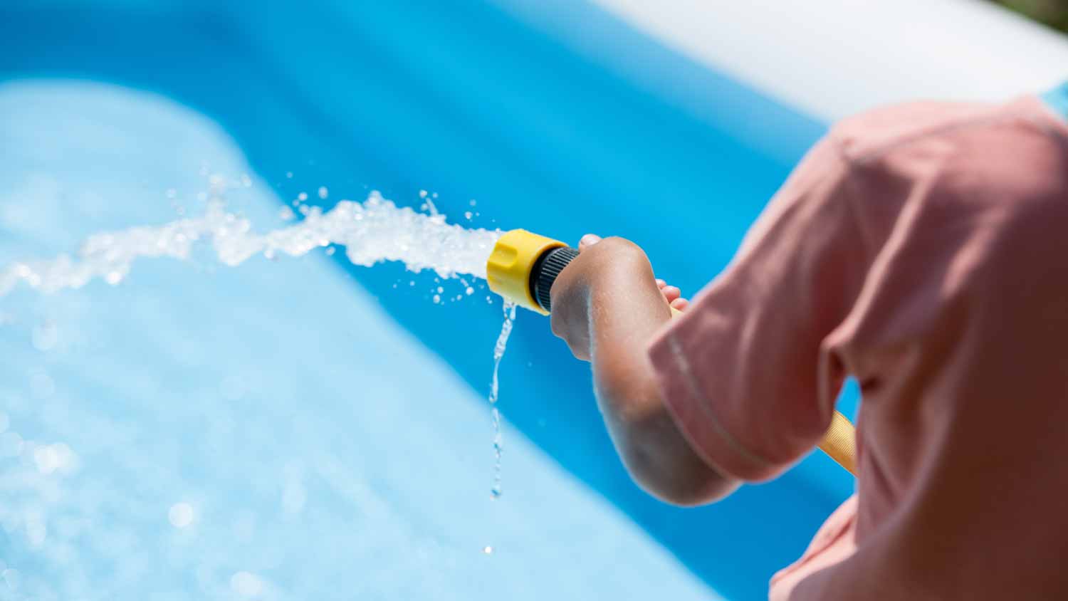 Boy filling up a paddling pool with a hose pipe