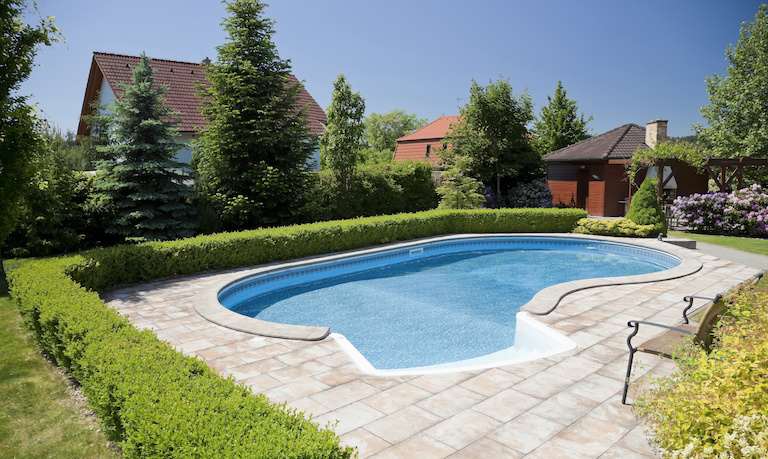home swimming pool with stone patio and shrubbery and houses in background