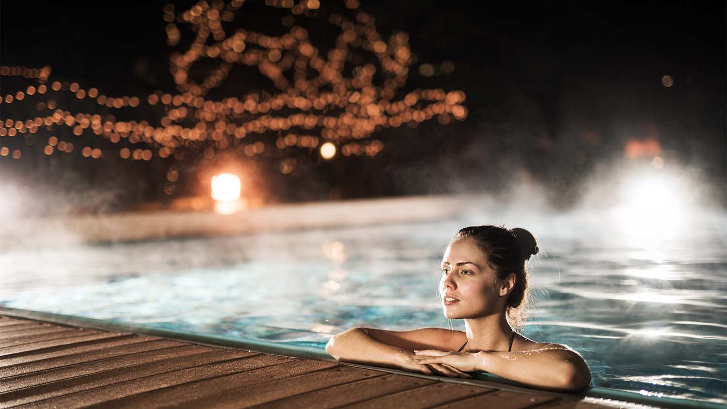 Young woman relaxing in heated swimming pool during winter night