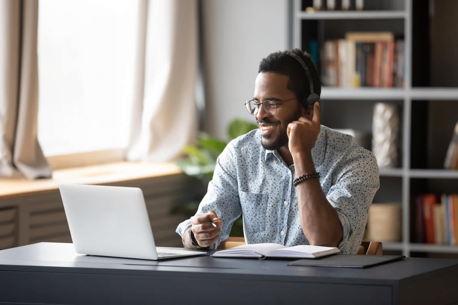 Man working from home in modern home office with glasses, headphones and a collared shirt