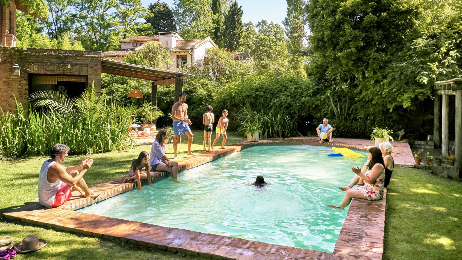 Family relaxing and watching children playing and swimming in backyard pool