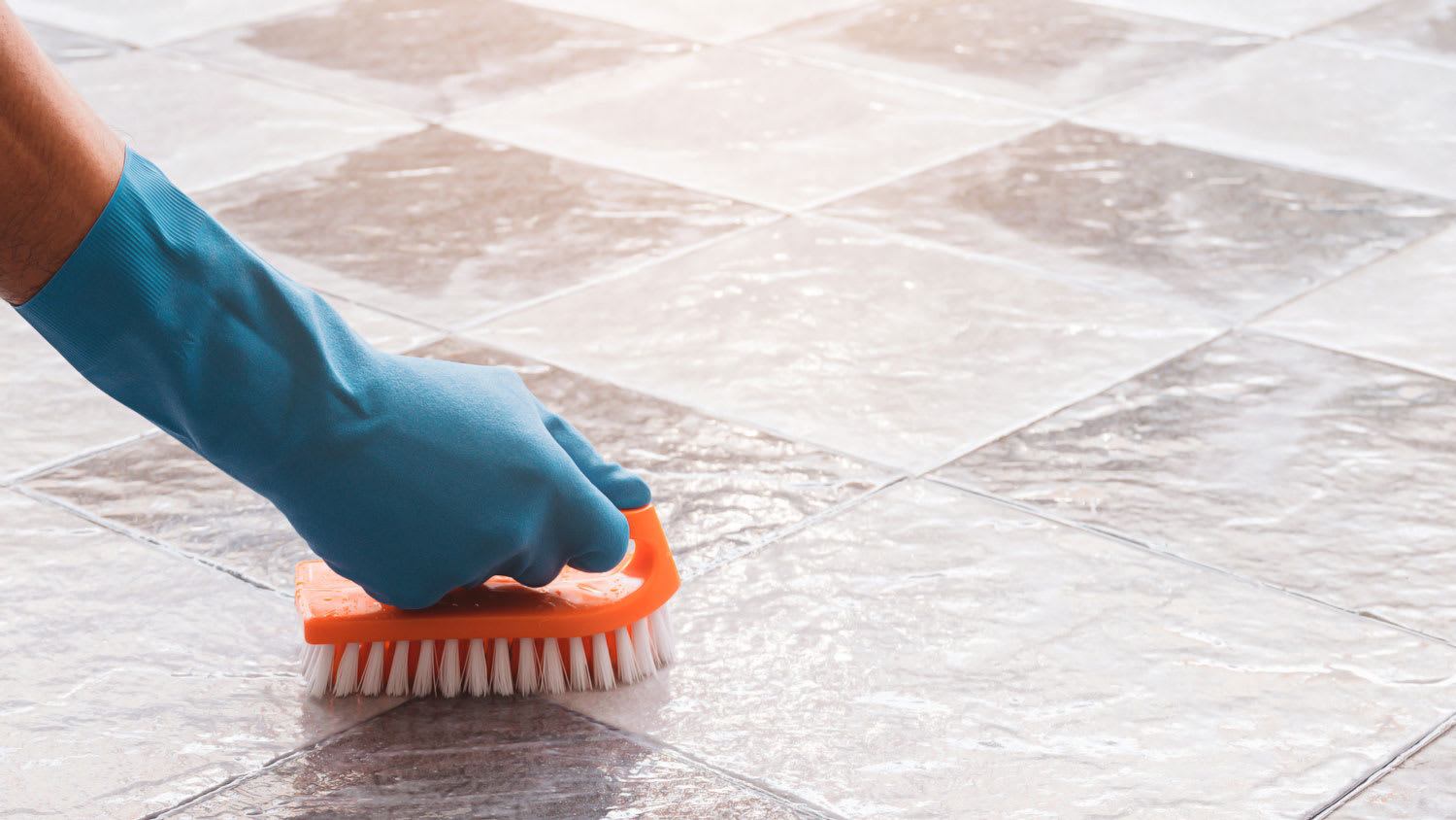 A hand scrubbing with a brush the grout on floor tiles