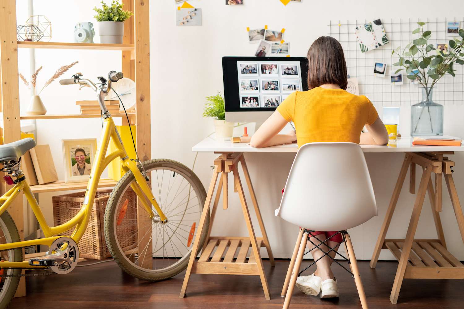 Woman with short brown hair working at her white desk facing her monitor in her home office that has a pop of yellow color