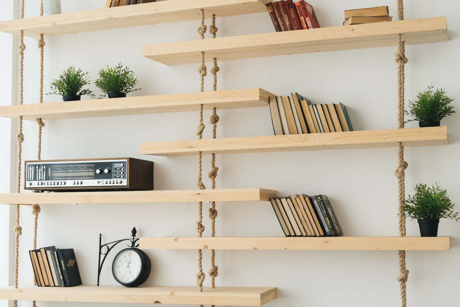 Handmade hanging wooden shelves against a white wall that display a book collection and small potted plants