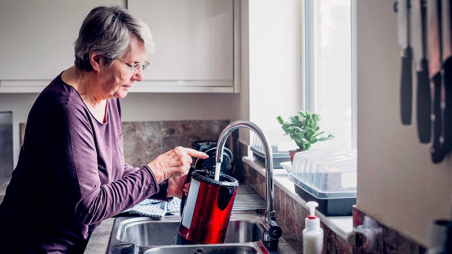 Woman using kitchen faucet to fill up kettle