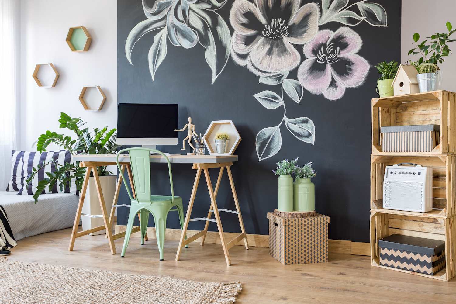 Chalkboard accent wall with large flowers drawn on it in a home office with a wooden desk and computer, shelves and a mint green metal desk chair