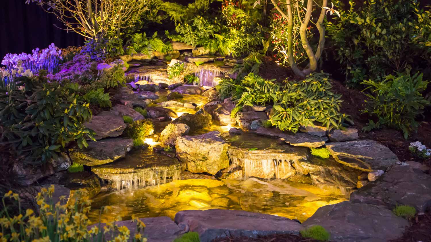 A view of landscaping with an illuminated waterfall