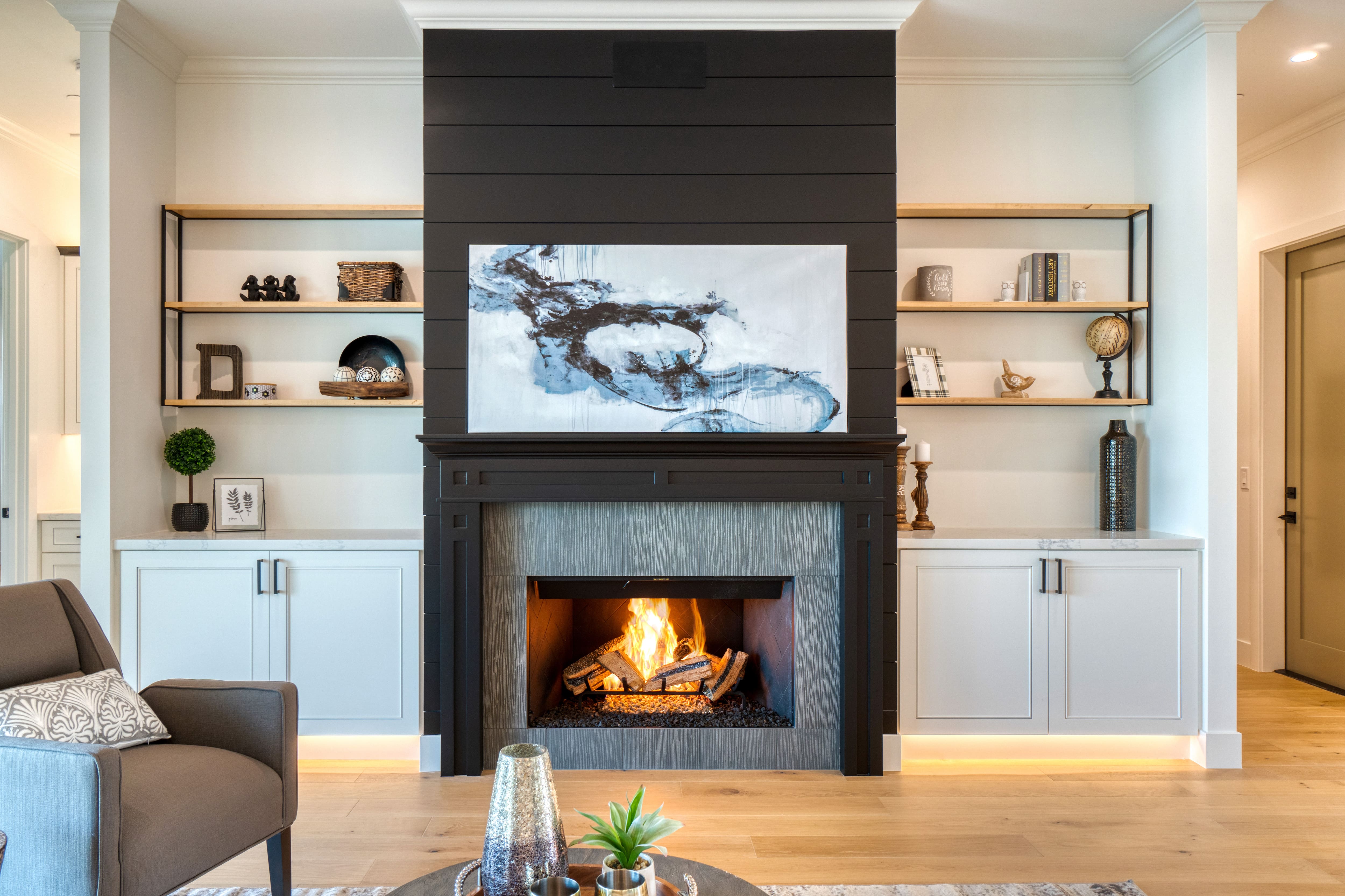 Luxury living room with black shiplap fireplace with abstract gray painting in front of white built-ins with wood shelves