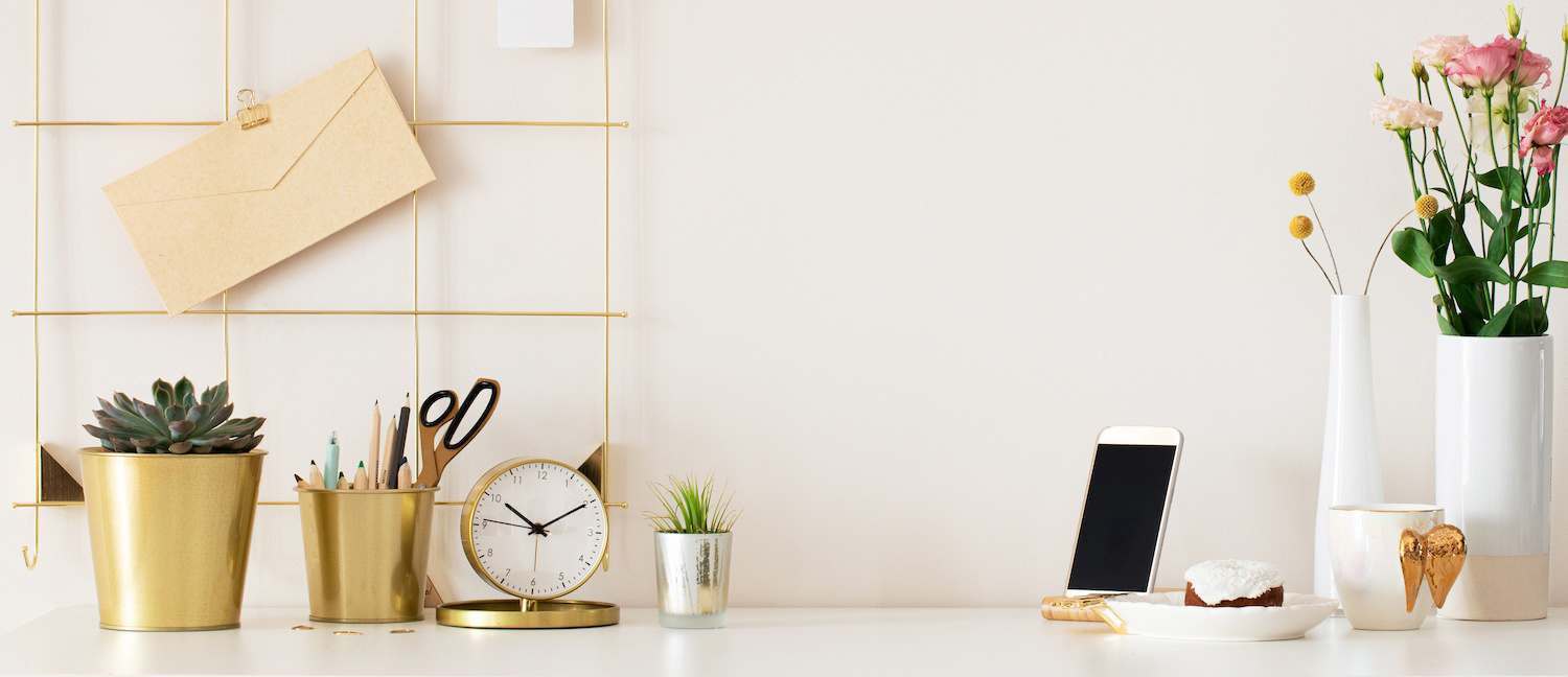 White desk and wall with stylish gold office supplies and flowers in white cases
