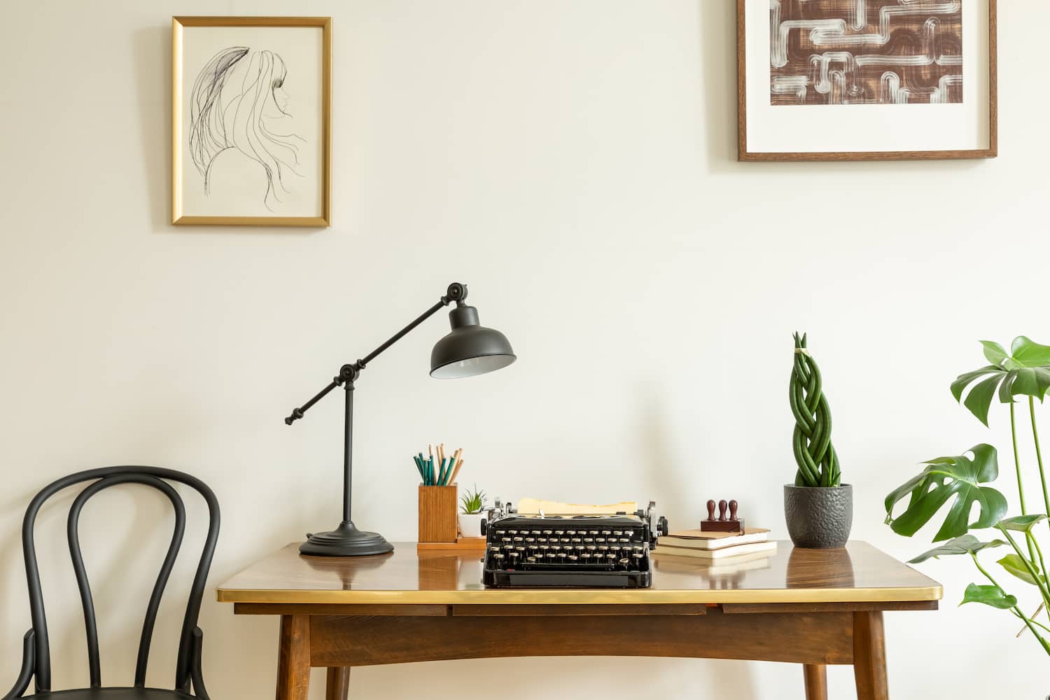 Minimalist home office with an antique wooden desk with a black desk lamp, pencil holder, vintage typewriter and plants