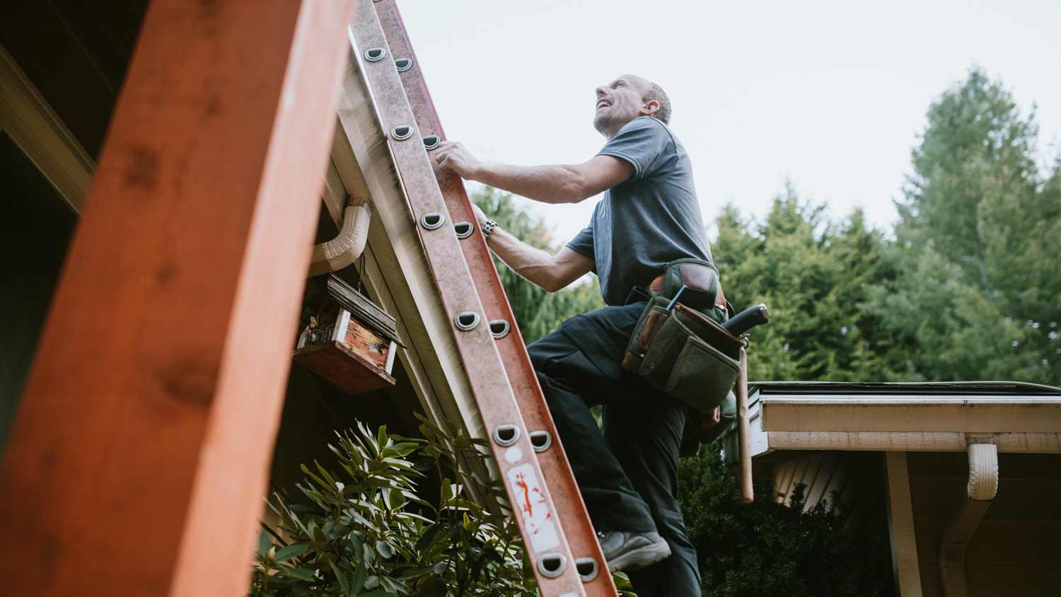 A contractor on a ladder checking a house’s roof