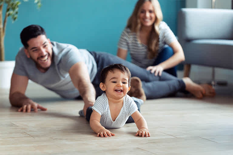 Baby excitedly crawling across the floor away from parents