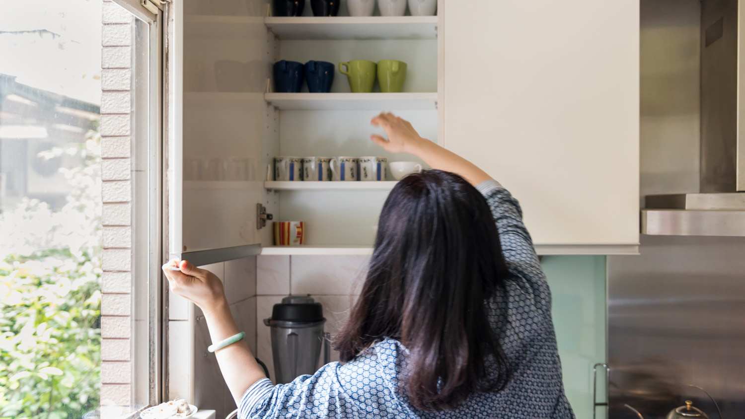 A woman grabbing a cup from a kitchen cabinet