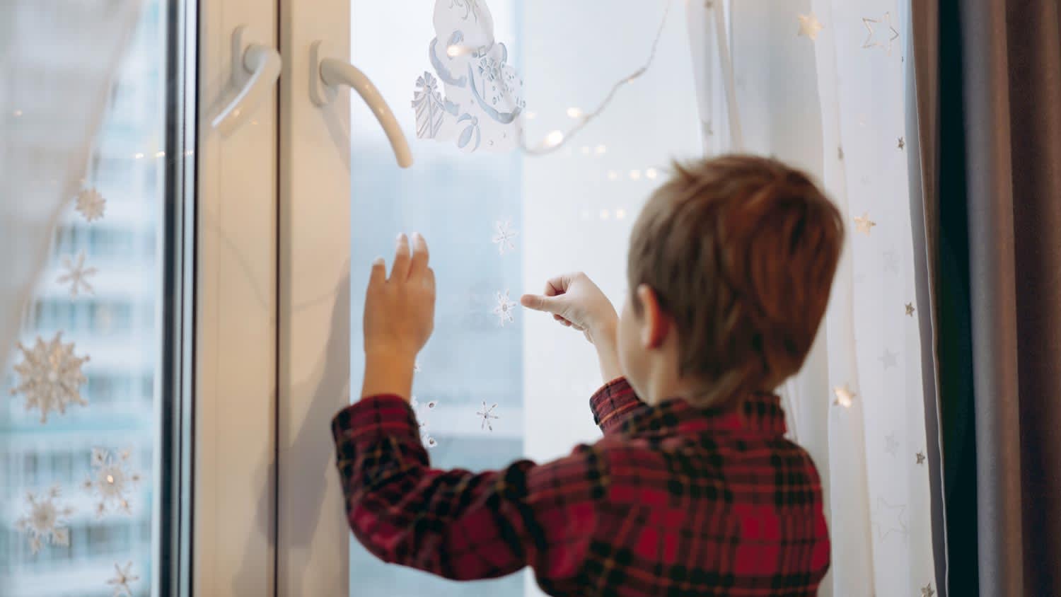 A kid decorating a window with Christmas stickers