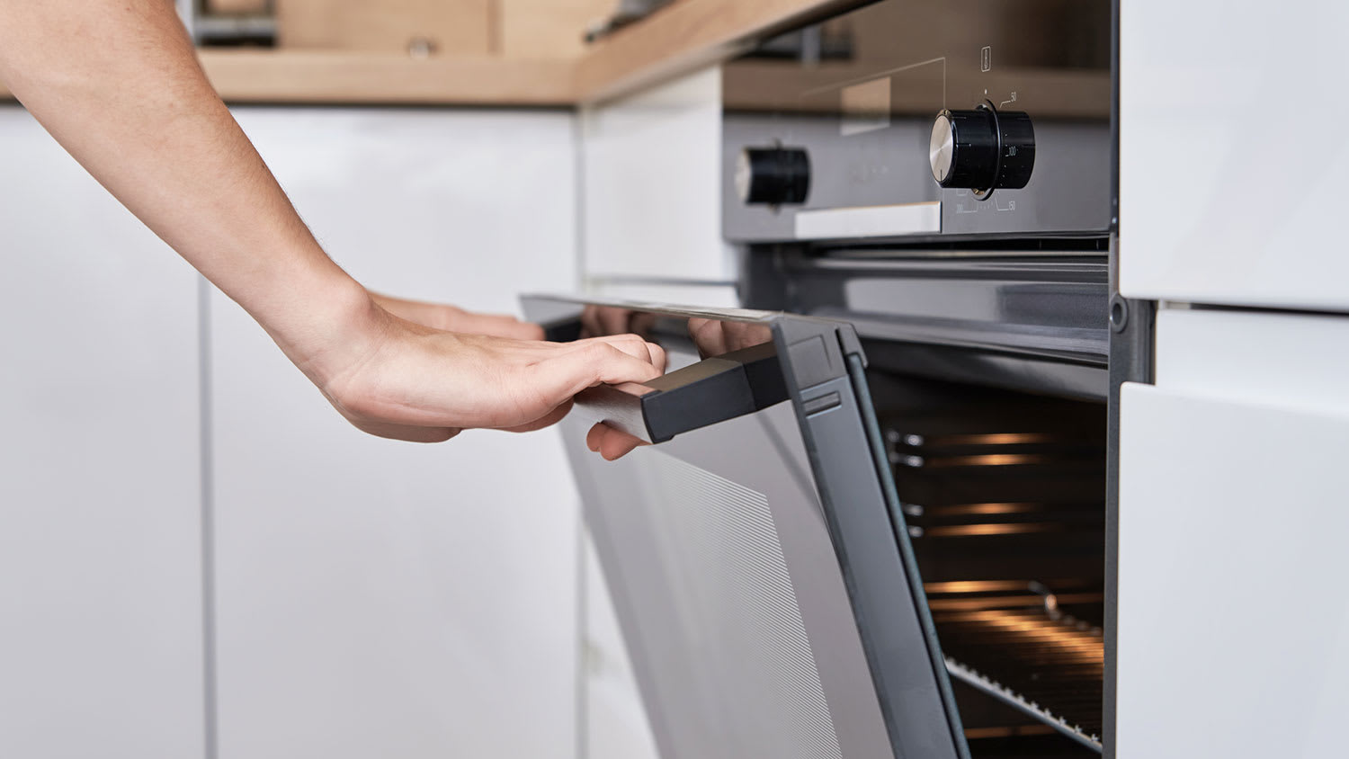 Hand opening the oven door in the kitchen