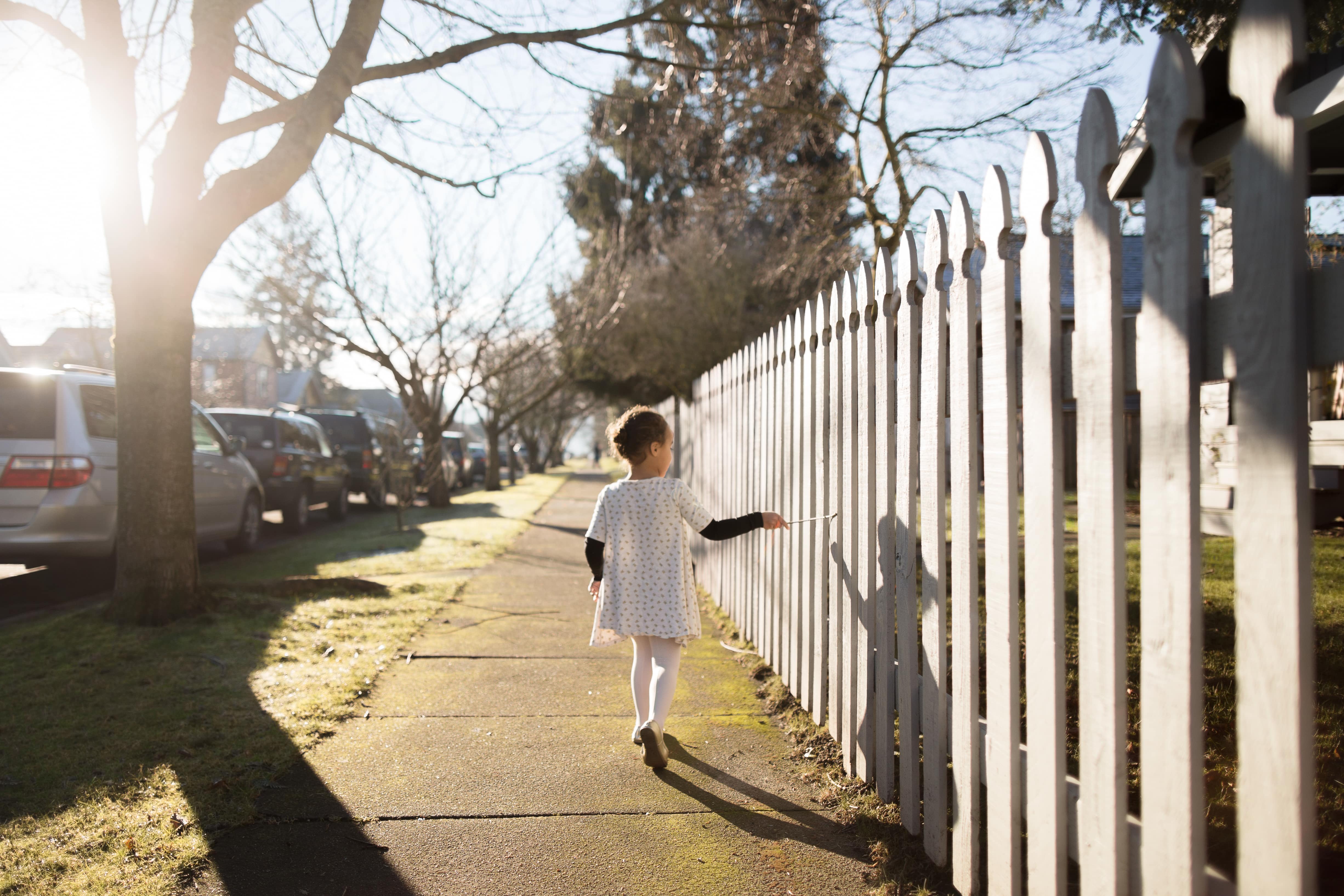 Girl walking next to white picket fence