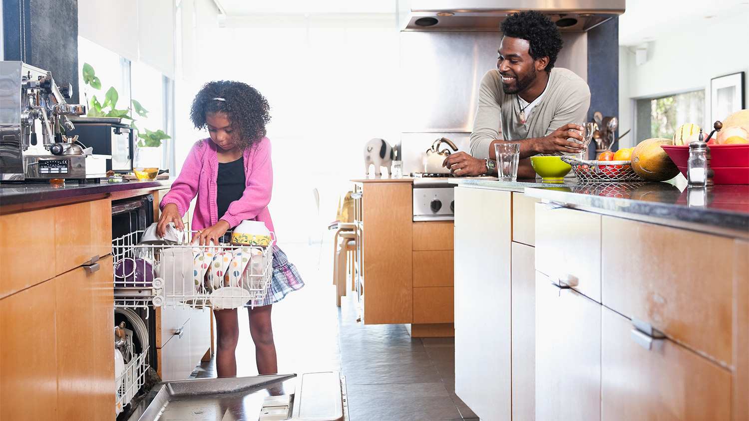 Father watching daughter loading dishwasher