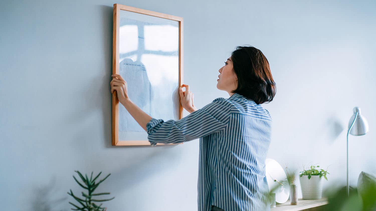 woman hanging picture on wall