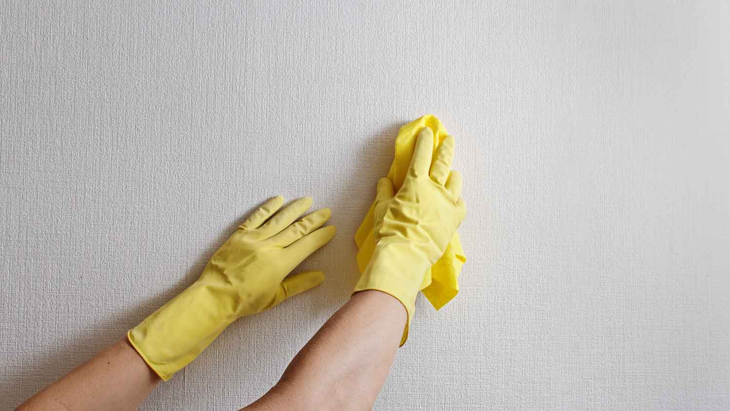 Hands in yellow gloves cleaning a white wall