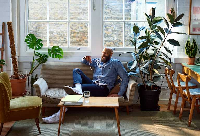 man sits on couch in living room next to rubber tree plant.