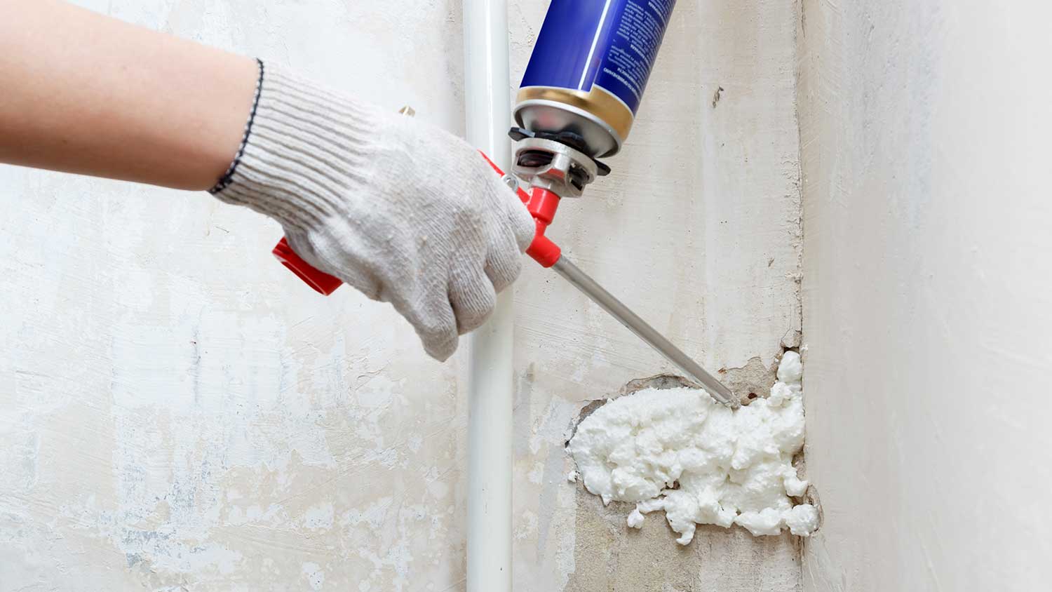Worker using polyurethane foam to fill a gap in the wall
