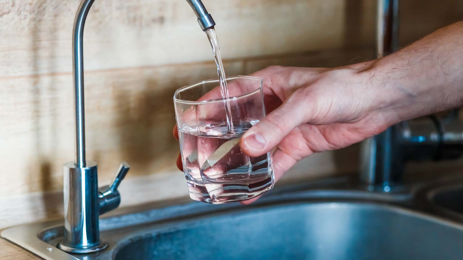 A man filling up a glass with water from a water filter faucet