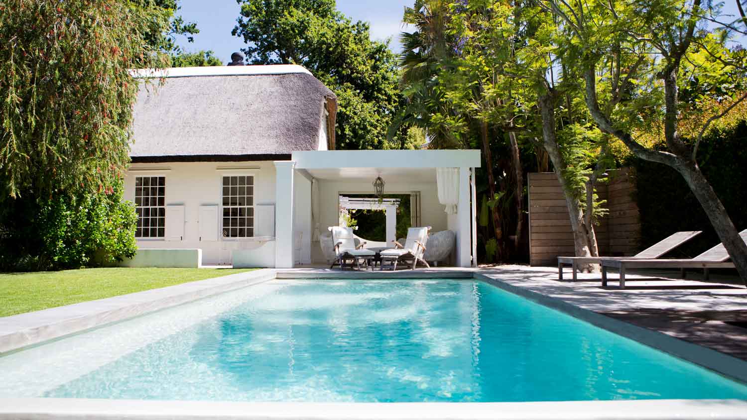 A pool in a lush backyard with some lawn chairs