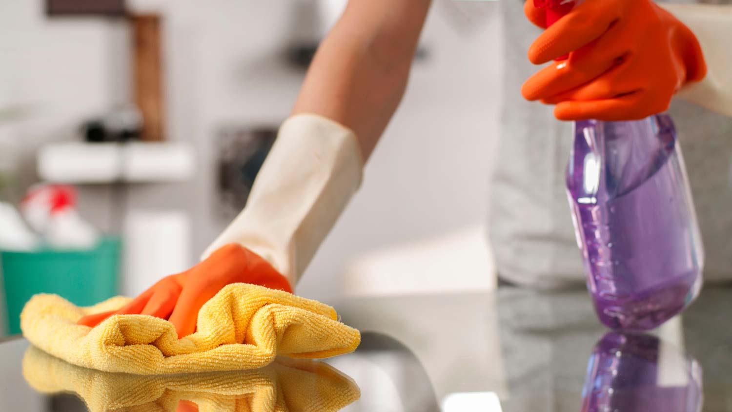 A woman in protective gloves cleaning a glass surface table