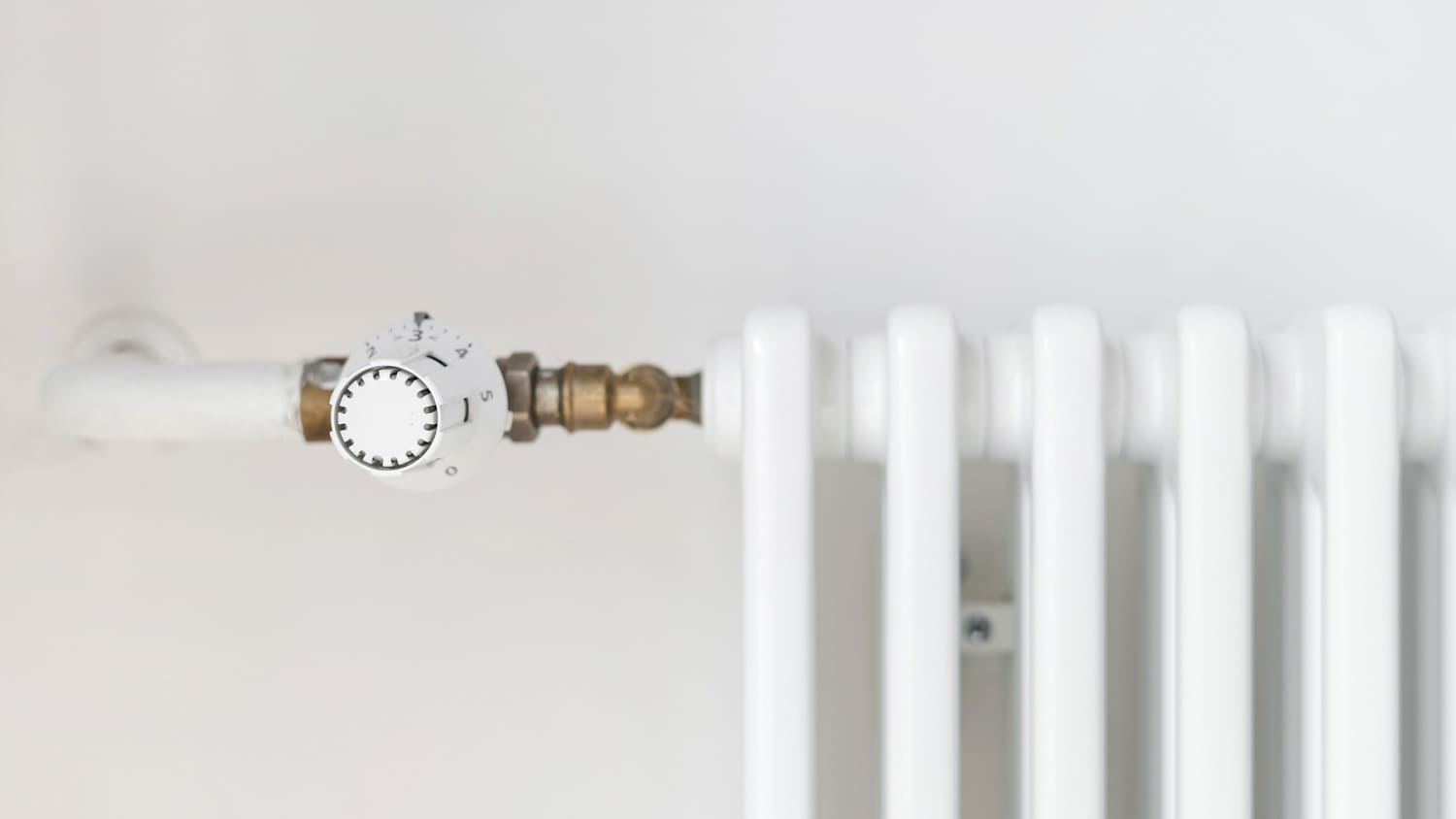 Close-up of a white radiator, its knob and the heating line