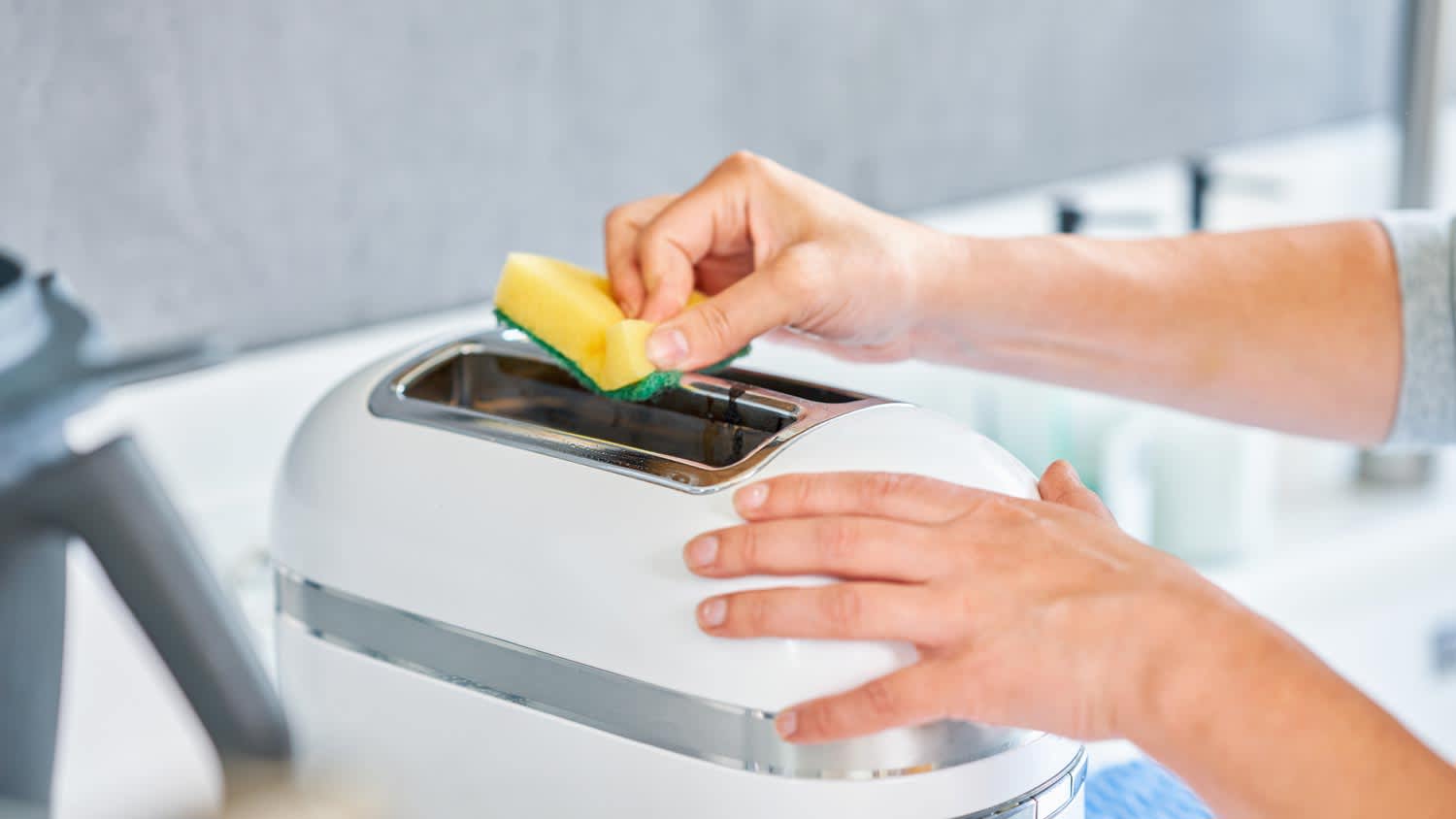 A woman cleaning with a sponge the exterior of a toaster