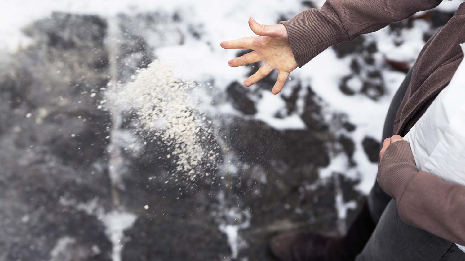 A man’s hand scattering salt in the driveway