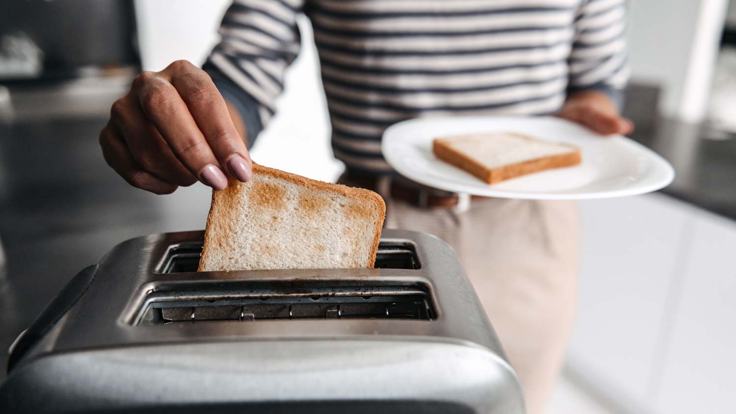 A woman picking toasted bread from toaster
