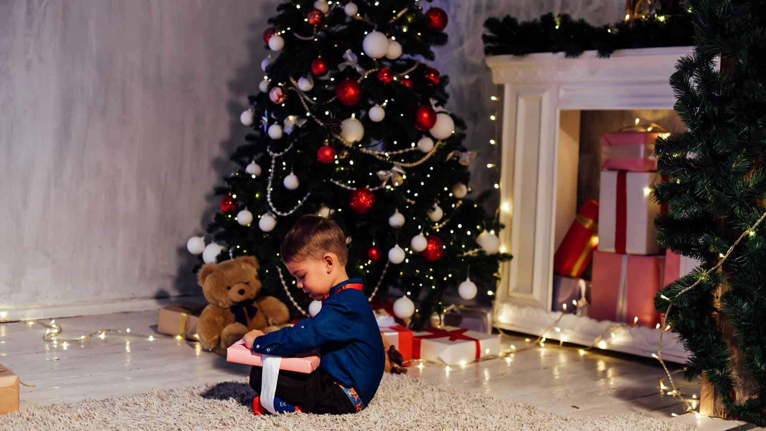 A kid opening a present in front of the Christmas tree