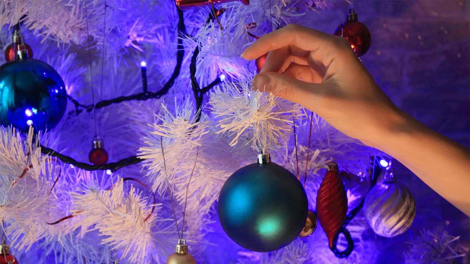 woman decorating white tree with colorful lights