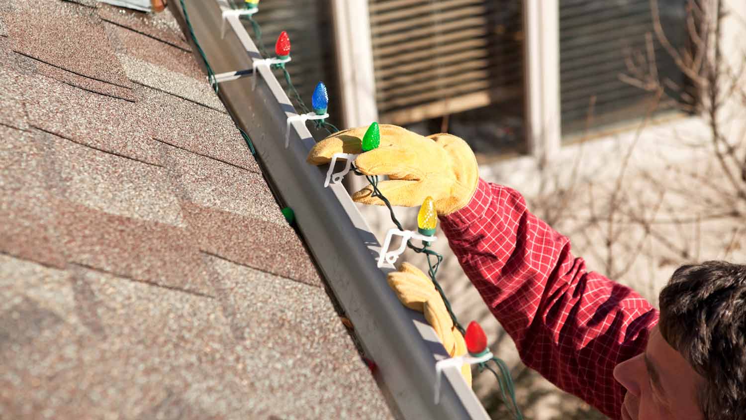 A man installing Christmas lights on the gutter