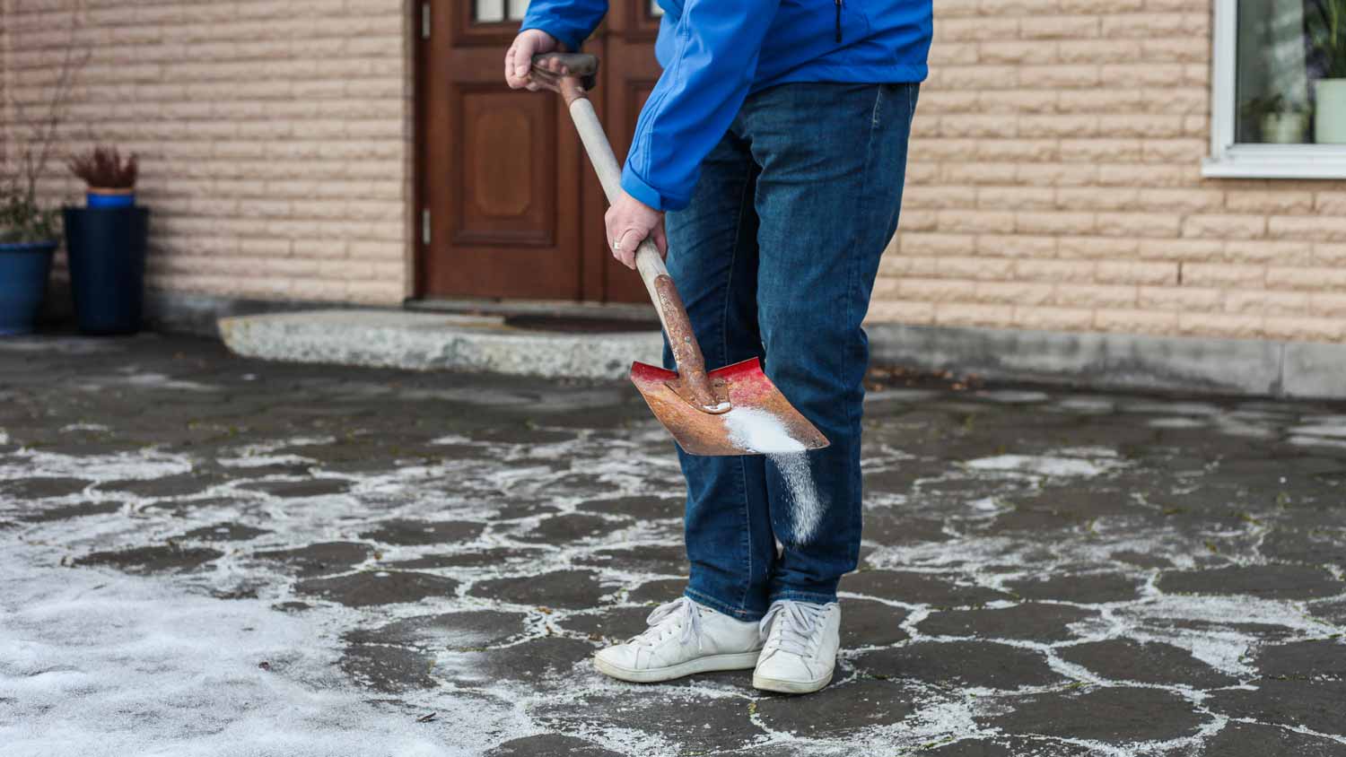 A man sprinkling salt with a shovel in the driveway