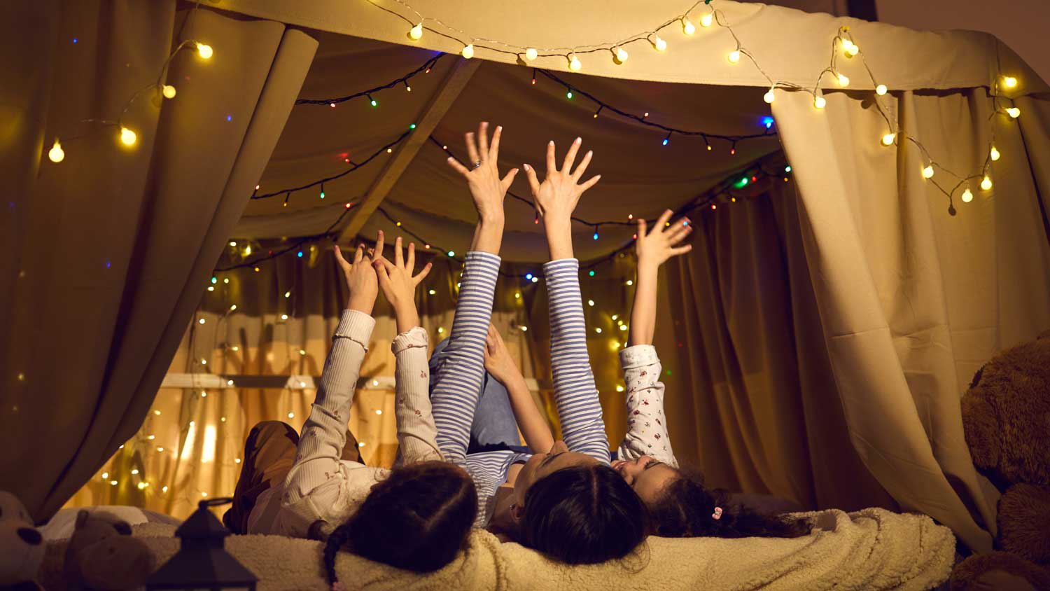 A mother laying with her children in a tent decotared with Christmas lights