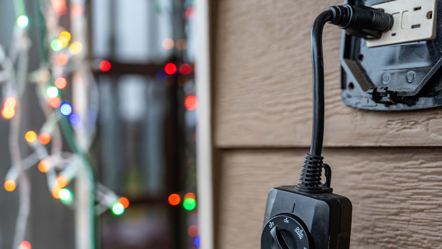 A GCFI outlet and an outdoor timer with Christmas lights in the background