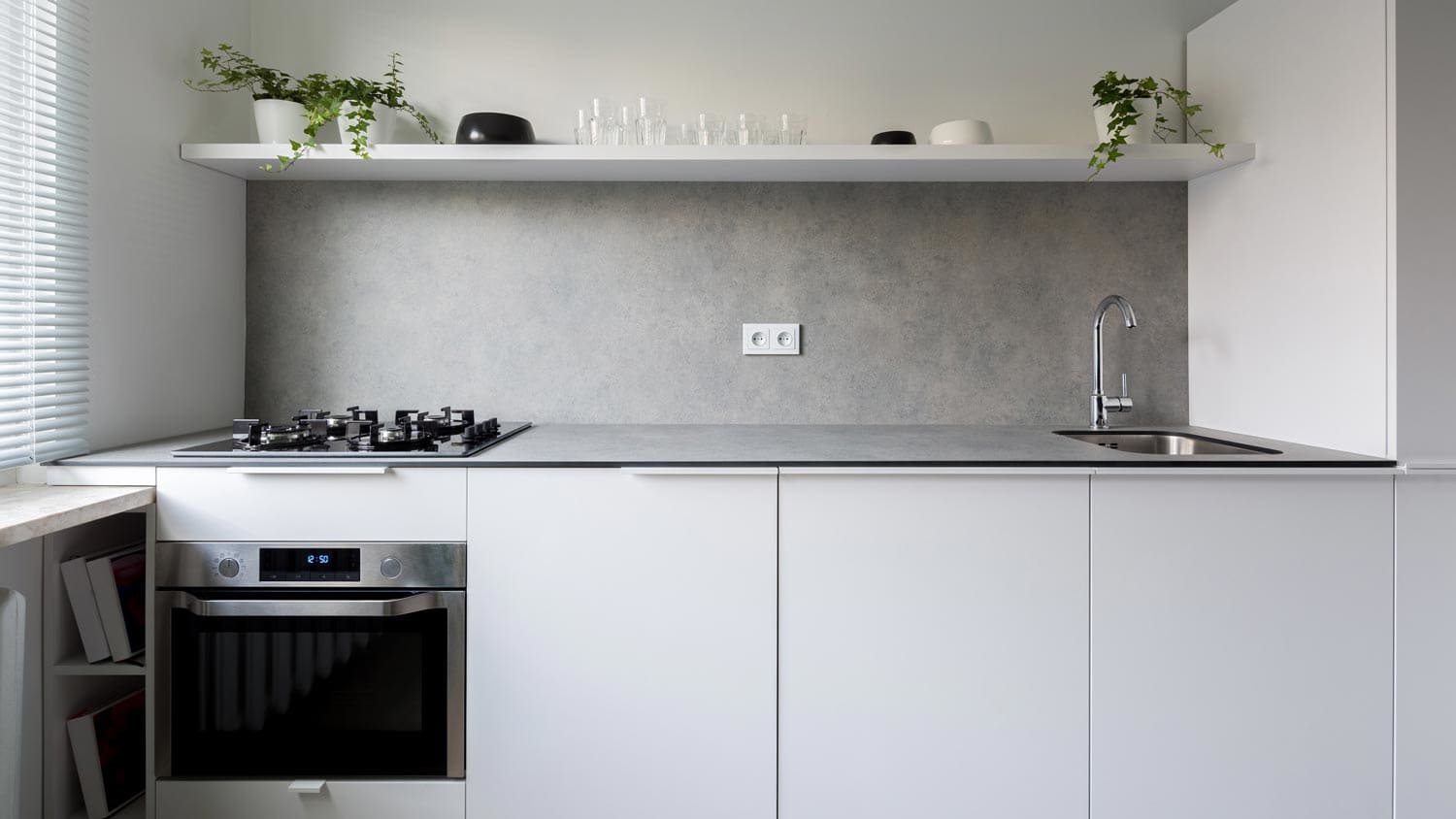 A mininal gray kitchen with a concrete backsplash